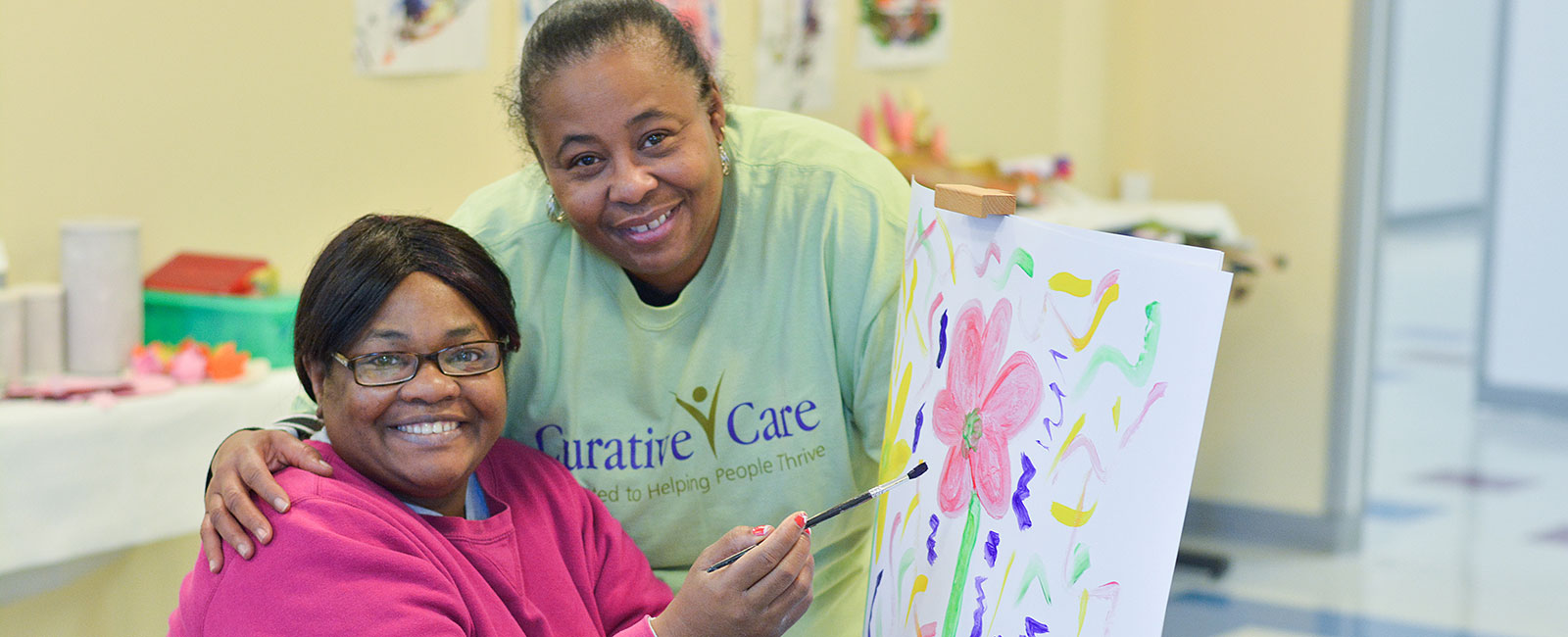 Adult female client painting a flower with employee caregiver